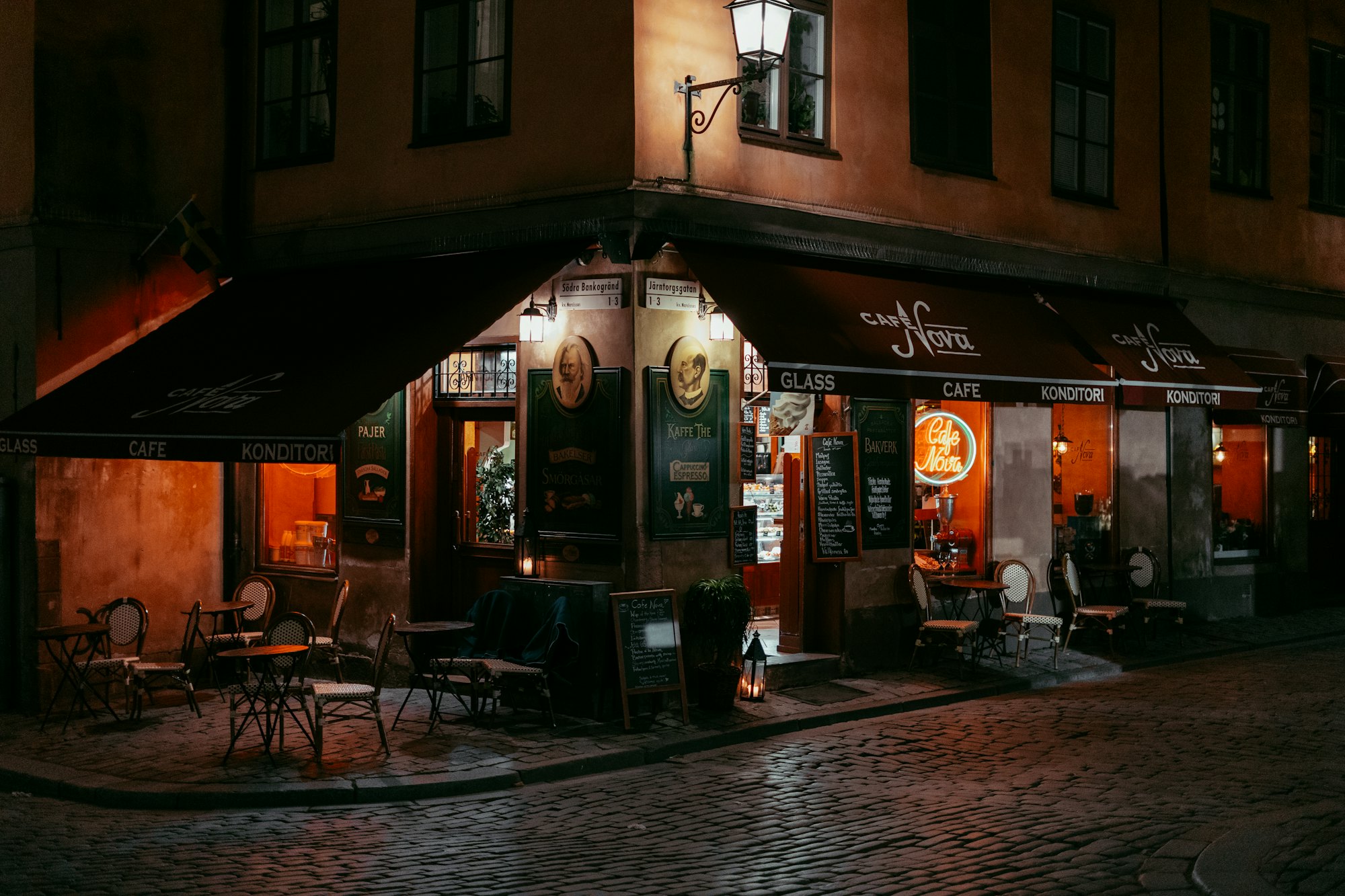 A European street corner at night, cafe awnings lit above wet cobblestones