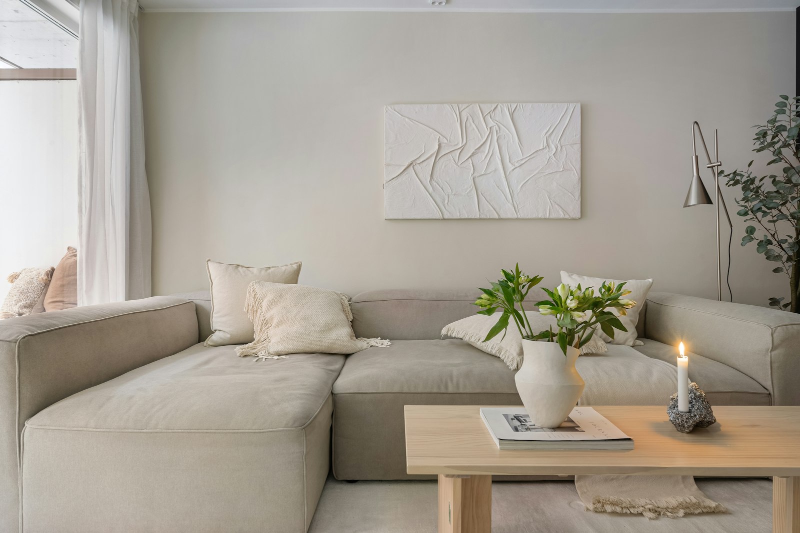 A quiet living room in warm neutral tones with a lit candle on a low table