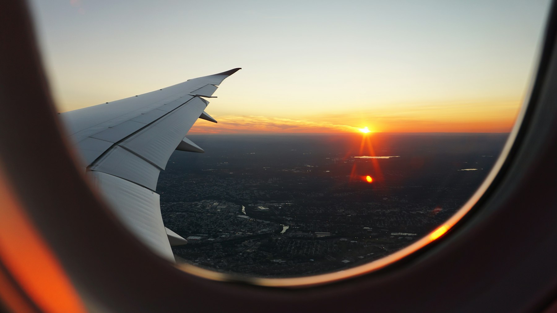 The wing of an aircraft seen through a cabin window at sunset